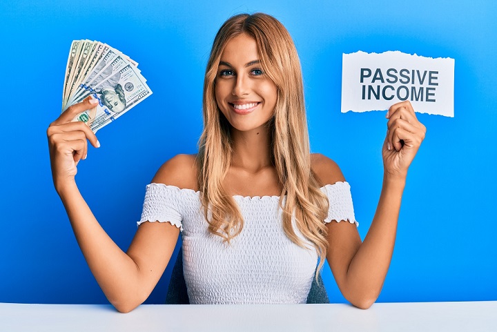 Beautiful blonde young woman holding dollars and passive income text smiling with a happy and cool smile on face. showing teeth.